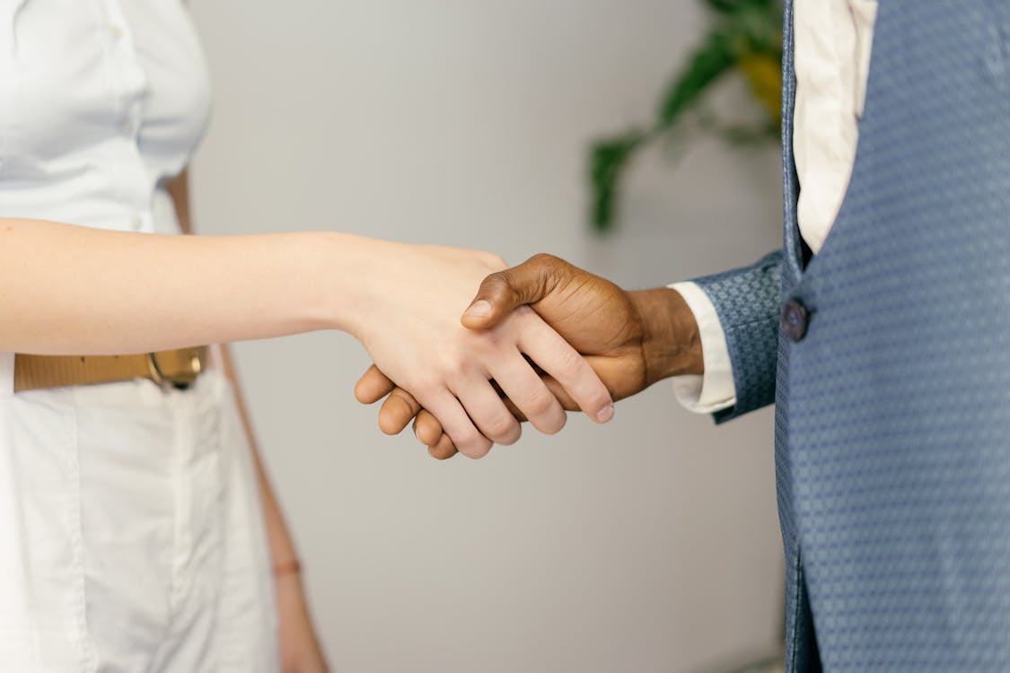 Two professionals in business attire shaking hands against a clean light background, representing a trusted B2B partnership