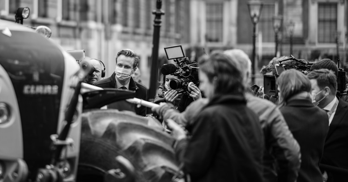 Journalists and camera crews gathered around a speaker at a press event on a city street