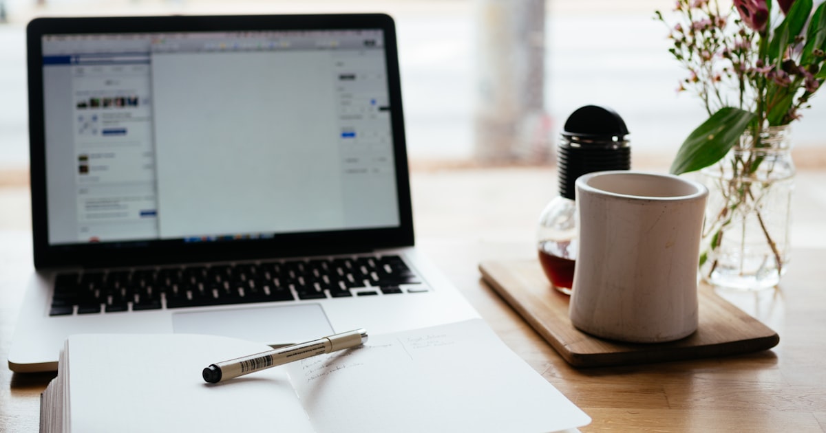 Open laptop next to a notebook and pen on a wooden desk, a writer's setup for content creation and publishing