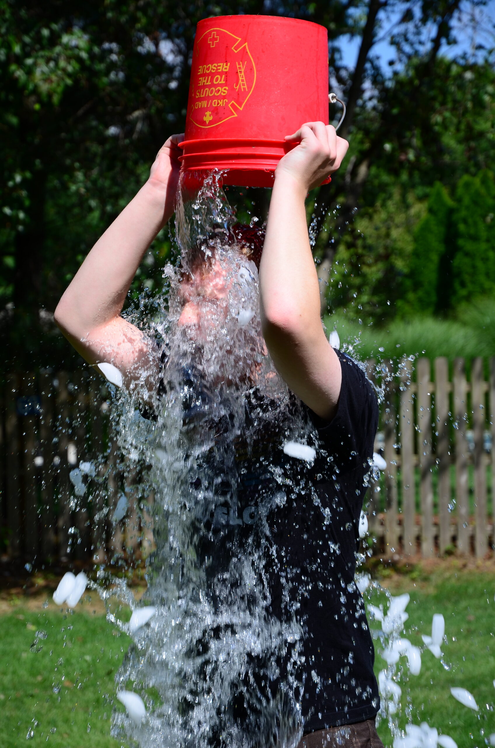 A person tipping a red bucket of ice water over their head during the ALS Ice Bucket Challenge
