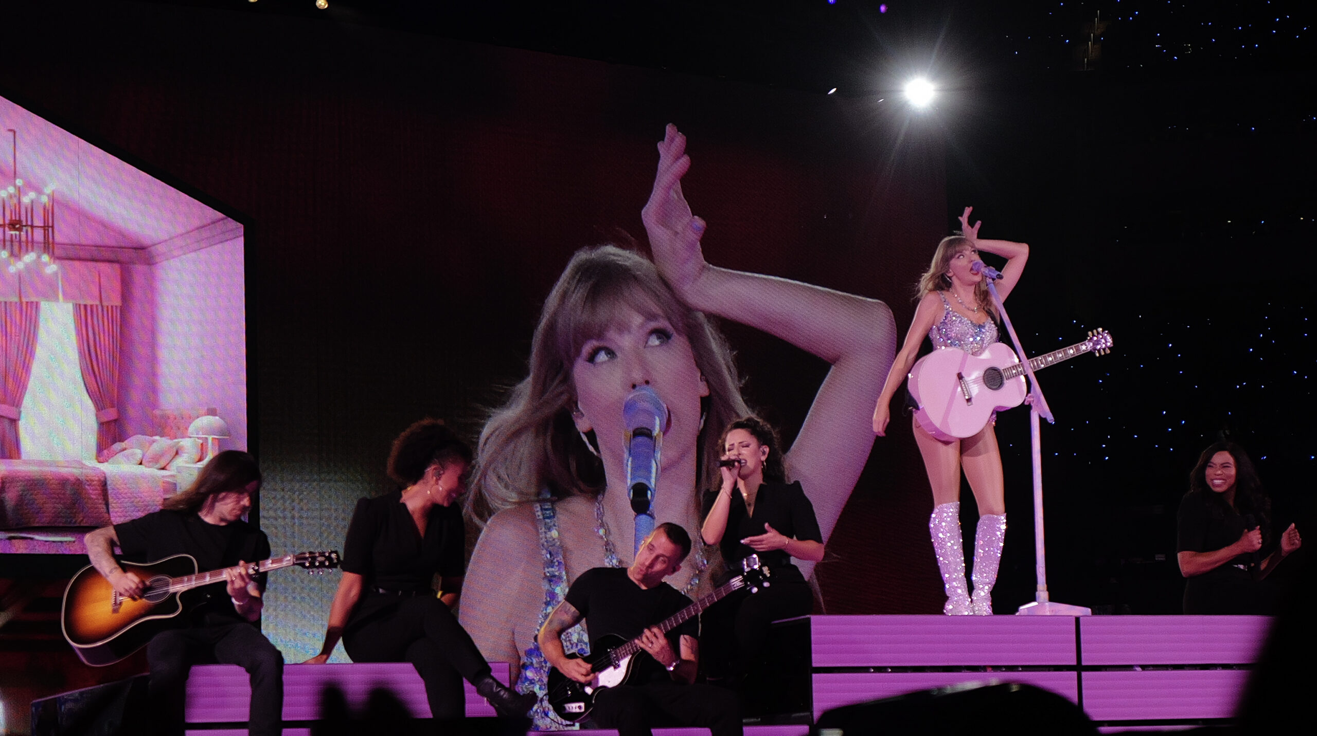 Taylor Swift performing on the Eras Tour stage in a sparkling bodysuit with a pink guitar