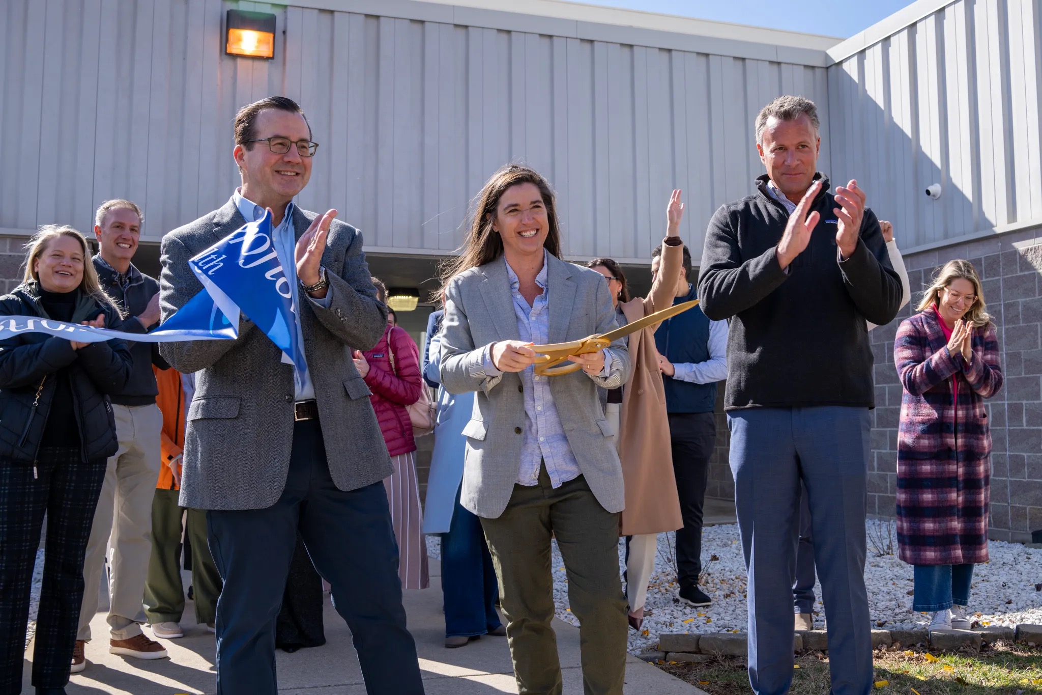 An Aeroflow ribbon-cutting event with executives applauding beside a branded banner and ceremonial scissors